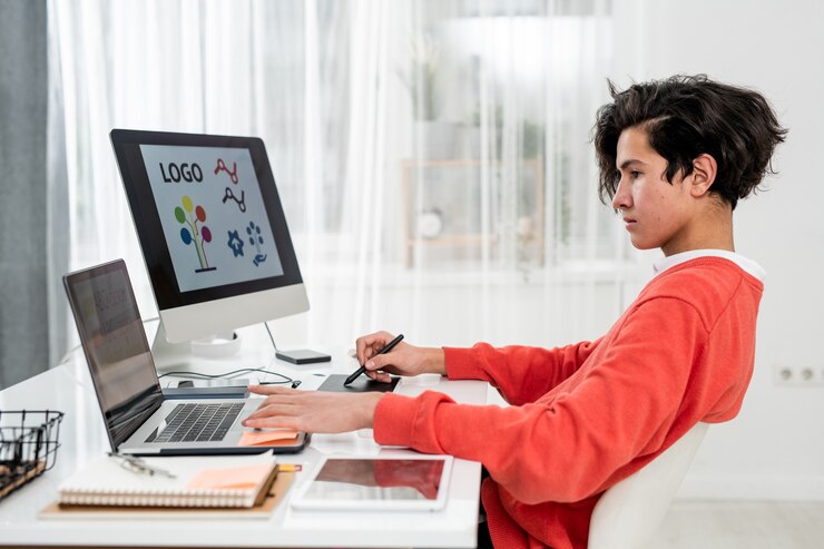 Young Freelance Designer Using Laptop While Sitting By Desk Front Computer Monitor Making Logo 274679 5244